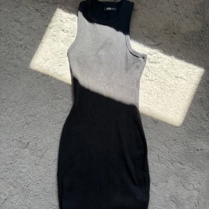 Svart och grå ribbad klänning FB Sister - Säljer en tight, ärmlös kortklänning från FB Sister i ribbad bomull. Klänningen har en snygg färgövergång från grått upptill till svart nedtill och rund halsringning.