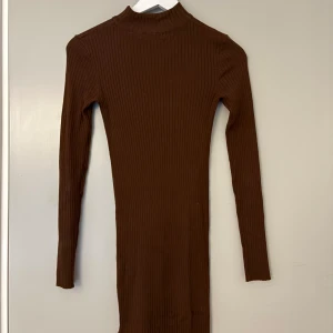 Brun ribbad långärmad kortare klänning - Snygg brun ribbad klänning med lång ärm och hög hals. Tight passform som framhäver figuren och ger en stilren look. Perfekt för dig som gillar minimalistisk stil och vill ha något bekvämt men ändå trendigt.