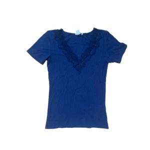 Blå ribbad topp med spetsdetalj - Mörkblå ribbad topp med korta ärmar och djup v-ringning dekorerad med spets. Snygg och enkel modell som sitter figurnära och passar perfekt till jeans eller kjol. Toppens material känns mjukt och stretchigt.