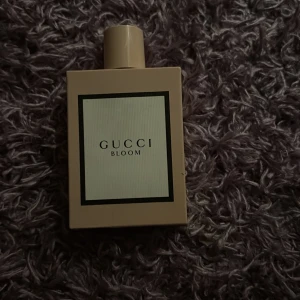 Gucci Bloom Eau de Parfum 100ml - Gucci Bloom Eau de Parfum i en stilren, ljusbeige, rektangulär flaska med svart-vit etikett. Flaskan rymmer 100 ml och har ett minimalistiskt uttryck med GUCCI-logga på locket. Perfekt för dig som gillar exklusiva och blommiga dofter.Fick den present men inte min still av parfym har testat bara och sen dess har stått på min smink bord 