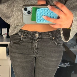 Lågmidjade jeans - Säljer ett par svartgråa jeans med slitna knän och klassisk femficksdesign. Jeansen har låg midja, Perfekta för en avslappnad och trendig look.