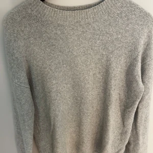 Grå stickad tröja från & Other Stories - Mysig grå stickad tröja från & Other Stories i storlek S. Tröjan har en klassisk rund halsringning och långa ärmar. Perfekt för lager-på-lager och chill dagar. Enkel att matcha med jeans eller kjol för en clean look.