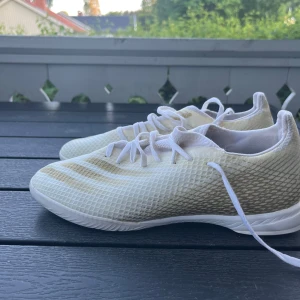 Vita fotbollsskor med snörning - Snygga vita fotbollsskor med diskret mönster och klassisk snörning. Skorna har en låg profil och ovandel i syntetmaterial med textur för bättre bollkontroll. Perfekta för dig som vill sticka ut på planen med stilrena skor.