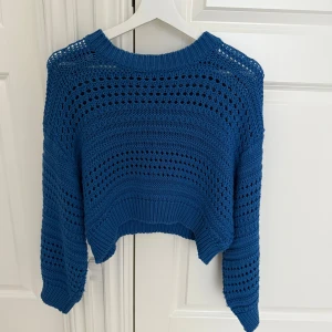 Blå stickad croppad tröja - Säljer en blå stickad tröja med croppad passform och lång ärm. Tröjan har ett snyggt hålmönster och bred ribbad kant nedtill och vid ärmslut. Perfekt för dig som gillar en chill och trendig stil.