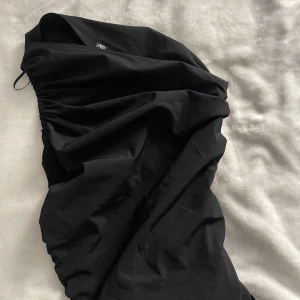 Svart tröja från Zara - Säljer en svart tröja från Zara med snygga rynkade detaljer längs sidorna. Tröjan har en tight passform och är tillverkad i ett mjukt material som känns bekvämt mot huden. Perfekt för dig som gillar minimalistisk och stilren look.