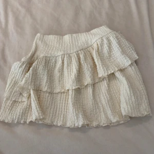 Volangkjol i beige från Gina Tricot - Supersöt kort volangkjol från Gina Tricot i beige. Kjolen har flera lager volanger och en bred resår i midjan. Materialet är strukturerat och känns lätt och luftigt, perfekt för varma dagar.