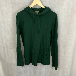 hoodie Polo Ralph Lauren - Mörkgrön hoodie från Polo Ralph Lauren med klassisk huva och snörning. Tröjan har lång ärm och är tillverkad i mjuk bomull. Diskret röd logga broderad på bröstet. Perfekt för en chill och stilren look. Storlek S, modellen är 185