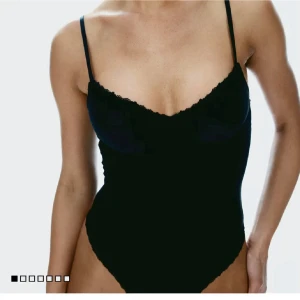 Svart spetsdetaljerad bodysuit - Supersnygg svart bodysuit med tunna axelband och v-ringning. Toppen har vadderade kupor och fina spetsdetaljer längs kanterna för en extra touch. Perfekt att styla med jeans eller kjol. Den är helt oanvänd och pris kan diskuteras. 