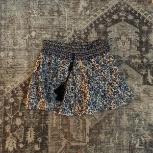 Blommig kortkjol från Zara XS - Supersöt kortkjol från Zara i blått och vitt med blommigt mönster. Kjolen har smock i midjan och dekorativa tofsar med pärlor framtill. Perfekt för dig som gillar boho-vibe och vill ha något luftigt och bekvämt.
