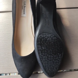 Svarta pumps från L.K. Bennett - Klassiska svarta pumps från L.K. Bennett med spetsig tå och låg klack. Skorna är tillverkade i mocka och har en elegant, tidlös design som passar perfekt till både jeans och klänning.