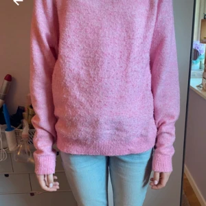 Rosa stickad tröja med lång ärm - Mysig rosa stickad tröja med lång ärm och ribbade muddar. Tröjan har en enkel och avslappnad passform, perfekt att slänga på sig till jeans. Färgen är ljusrosa och materialet känns mjukt och fluffigt.
