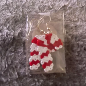 Juliga örhängen med polkagrisar - Söta örhängen formade som polkagrisar i rött och vitt. Perfekta accessoarer för att sprida julkänsla! Gjorda av pärlor i klassiskt randigt mönster och med silvriga krokar.