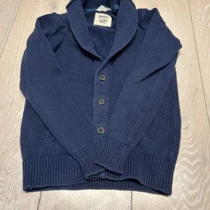 Mörkblå stickad kofta Stockholm - Mysig mörkblå stickad kofta från Stockholm med bred krage och knäppning framtill. Koftan har långa ärmar, ribbade muddar och två fickor. Perfekt för lager-på-lager och chill dagar. Den är i storlek 152 men passar lite större men max längd skulle jag säga är 157 cm. Tveka inte för att höra av er kan gå ner i pris vid snabb affär. Hör av er om flera bilder om de skulle behövas😊