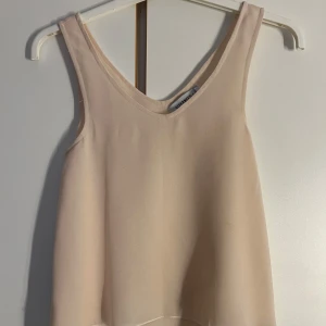 Beige linnetopp från Size & Needle - Supersöt linnetopp från Size & Needle i flowy, dubbellager tyg. Toppen har v-ringning och är ärmlös, perfekt för en chill och stilren look. Lätt och luftig känsla, passar grymt till jeans eller kjol.