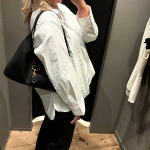Svart axelväska med gulddetaljer - Snygg svart axelväska i stilrena guldfärgade metalldetaljer. Väskan har en mjuk, något trekantig form och bred axelrem som gör den bekväm att bära. Perfekt storlek❤️‍🔥❤️‍🔥