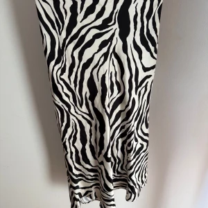 Zebramönstrad långkjol i satinlook från BikBok - Snygg långkjol med svartvitt zebramönster och lätt glansig satinlook. Kjolen har en rak passform som sitter skönt på höften och faller snyggt längs benen. Perfekt för dig som vill sticka ut med ett djurmönster. Tyvärr har jag råkat komma åt och riva upp några sömmar, dock något som tackvare mönstret inte är så synligt!