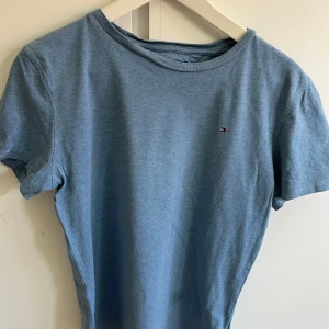 Blå t-shirt från Tommy Hilfiger - Snygg blå t-shirt från Tommy Hilfiger med liten broderad logga på bröstet. Klassisk rund halsringning och korta ärmar. Tillverkad i mjuk bomull som känns skön mot huden. Perfekt för en chill och stilren look.