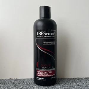 TRESemmé Colour Revitalise Schampo - TRESemmé Colour Revitalise schampo i svart plastflaska, 500 ml. Speciellt framtagen för färgat eller slingat hår med UV-filter och nutri-olja för att skydda färgen och ge glans. Snygg design med röd och silverdetalj på etiketten. Säljer både schampoo och balsam. Oanvända båda två.