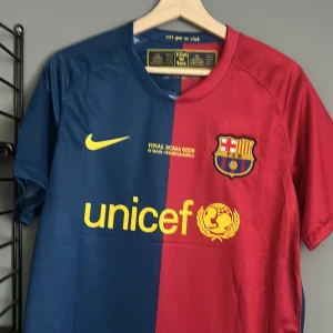 FC Barcelona Henry 14 Finaltröja Nike - Säljer en ikonisk FC Barcelona fotbollströja från Nike, Final Roma 2009 edition med Henry 14 på ryggen. Tröjan är blå och röd med gula detaljer, klubbmärke och Unicef-tryck framtill. Tillverkad i lätt och ventilerande polyester, perfekt för fans. Helt ny med tagg en replika 