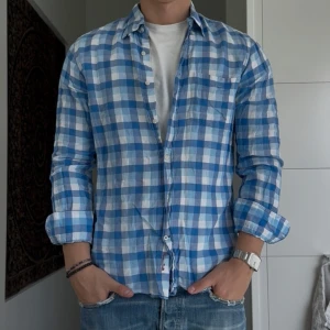 Blåvit rutig skjorta Massimo Dutti - Snygg rutig skjorta från Massimo Dutti i blått och vitt. Skjortan har klassisk krage, långa ärmar och knäppning framtill. Tillverkad i mjuk bomull och har en broderad logga vid knappraden. Perfekt till jeans för en chill look.