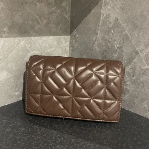 Brun handväska  - Säljer söt liten brun handväska i nyskick  för 40kr, har tyvärr tappat bort kedjan därav priset. Funkar perfekt som hand clutch. Fraktas på köparens bekostad. 