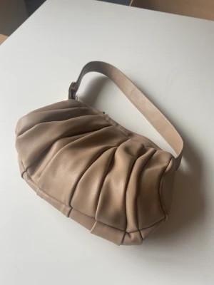Mango väska - Beige väska från Mango i baguette-modell. Lite skrapningar på den guldiga färgen på spännet men annars i mycket fint skick.