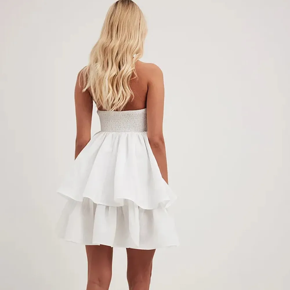 Säljer nu dennna super fina vita volang bandeau klänningen från NA-KD som nästan alltid är slutsåld. Strl 38 men skulle säga att den är lite större en en ”vanlig” 38. Perfekt till studenten, konfan eller sommar. Helt ny, med lapp och allt kvar🤍. Klänningar.