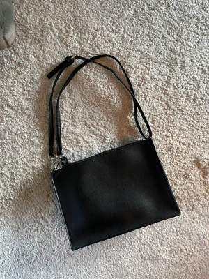Svart axelväska - Svart axelväska i väldigt enkel design! Superpraktisk och passar till allt. Väskan har fyra mindre fack inuti och bandet har jag vikt dubbelt för att kunna ha den som axelväska. Hör av er om ni har några frågor!🖤