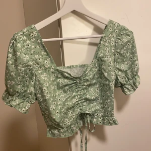 Grön topp med blommor och snörning - Supersöt topp med lite volym i är ärmarna och snörning samt stretchigt mesh-material i ryggen. Aldrig använd