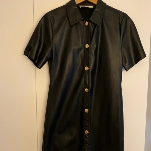 Svart skinnklänning med knappar M - Svart skinnklänning med krage och knappar. Storlek M men är lite mindre så passar som S. 