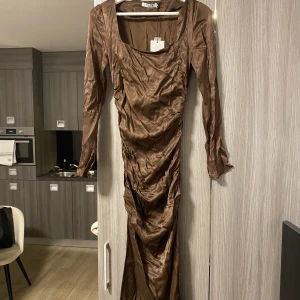 Brun klänning 32 - Oanvänd fodralklänning i satin från nakd. Säljes pga fel storlek