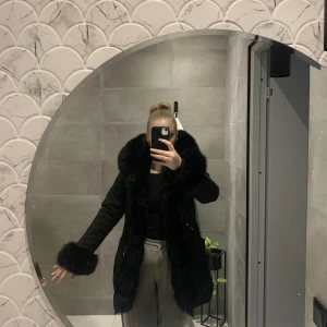 Svart vinterjacka - Pälsen på huvan och armarna är äkta och går att ta bort och sätta på som man önskar.  Jag är ca 169cm lång och går under rumpan.  Jackan går att stänga med knappar och dragkedja går även att dra åt i midjan. Defekt finns. För mer info/bild kontakta mig🥰  