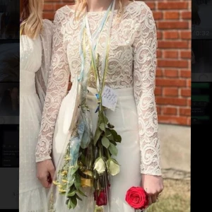 Vit jumpsuit med spets  - Säljer nu min fina jumpsuit jag hade på avslutningen i 9an. Använd en gång av mig och använd nån gång av en annan tjej. Den är sydd i ryggen så den ska sitta lite tajtare och i längden, jag är 173cm med långa ben och den sitter perfekt i längden. Har även sytt till den beiga delen vid bysten så den sitter fast då den åkte ner. Det är en öppen rygg men dragkedja där bak. Lite genomskinlig men ett par vita/hudfärgade underkläder eller hudfärgade strumpbyxor gör susen. Pris kan diskuteras 