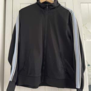 black track top with blue details on sleeves. two side pockets. zip closure at the front.