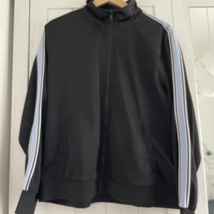 Monki track top in black - black track top with blue details on sleeves. two side pockets. zip closure at the front.