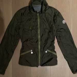 Moncler jacka - Höstig tunn monclerjacka! Fin mörkgrön färg med lite ljusare militärgröna detaljer. Har en liten fläck på insidan av ryggen, men inget som syns när man har på sig den! Storlek 1- skulle säga att den passar en XS. Figursydd och lång i ärmarna. 
