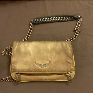 Zadig Voltaire väska - Säljer nu denna guldiga lite slitna men fortfarande användbara Zadig väskan, Zadig papper och box ingår,ett pyttelitet hål på innersta hörnet som man inte märker❤️köpt på NK,bara att höra av er vid frågor/intresse TRYCK EJ PÅ KÖP NU❤️🙅‍♀️ postar spårbart☺️