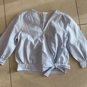 Omlott skjorta - Fin blårandig skjorta från H&M. Knyter i midjan, omlott. Mycket bra skick, väldigt elegant. 