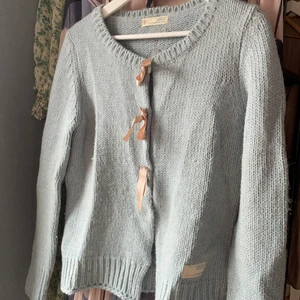 Odd Molly Kofta - Ljusblå stickad kofta från Odd Molly. Stängs med knappar som är dekorerade med rosetter. Använt skick med två små fläckar. Storlek 2, motsvarar M. 