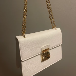 Vit justerbar väska med guld detaljer  - Använd en gång, köpt på new yorker för 250kr. Väskan går att justera vid axelbandet, den har väldigt mycket förvaring inuti! (Väskan är i väldigt bra skick)  Köparen står för frakten💖