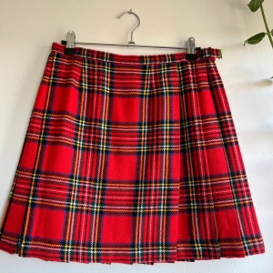 Rutig plisserad kjol - Rutig omlottkjol av ullblandning. Stängs med spänne i sidan och knapp på insidan. Knappen kan lätt flytas för att reglera midjemåttet. 36cm mätt över midjan, 42cm lång. 