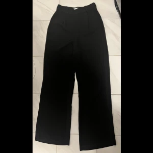 Svarta kostymbyxor - Svarta kostymbyxor, de är wideleg och straightleg (alltså raka i modellen) tyget är inte vanligt kostymtyg utan ett flowy tyg som formar kroppen. Långa i benen! Dragkedja finns på sidan. Stl 36