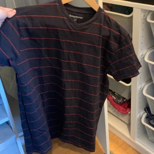 V ringad T-shirt  - En marin blå v ringad T-shirt med tunna röda ränder. I storlek M. Står ej för frakten