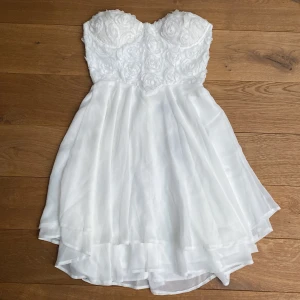 Vit klänning med rosor  - Klänning från Te Amo🤍 Aldrig använd. Lappen och allt sitter kvar. Det finns även genomskinliga axelband i en liten påse som man kan sätta fast (andra bilden). Storlek: 8 (vilket verkar motsvara 36).