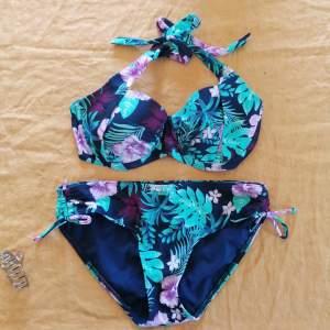 Marinblå bikini med mintgröna och ljusrosa blad/blommor. Bra support i toppen med bygel. Från warp (stadium), knappt använd, bra skick. 