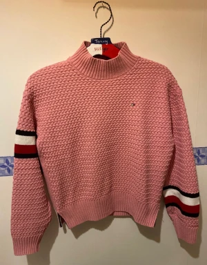 Tommy Hilfiger sticks tröja i toppenskick! - Rosa polotröja med kabelstickning med exklusiva detaljer och fin kvalitet  Märke: Tommy Hilfiger   Skick: Mycket fint skick, knappt använd  Nypris: >900kr