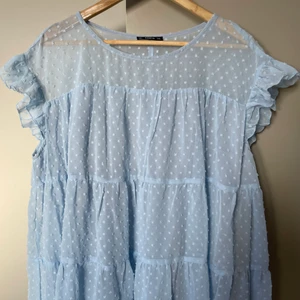 Blus  - Aldrig använd. Ljus blå. Dubbelt tunnt tyg. Det övre är prickigt. Vid modell. Volang vid axeln. 