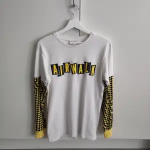 Vit långärmad t-shirt med gul- och svartrutiga ärmar. Unisex storlek medium. Märket är Airwalk men köpte den på Depop för några år sen. Det är en ljus fläck på vardera ärm men syns knappt när tröjan är på 🙂 