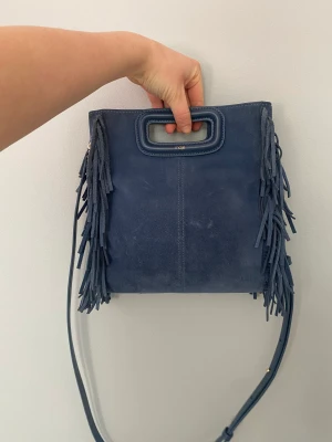 Maje väska  - Säljer min blåa Maje väska då jag inte använder den långre. Pga den blå färgen och mocka materialet så finns det tyvärr tecken på användning men det kan säkert åtgärdas. Köpt för 2500kr i Maje butiken 2021