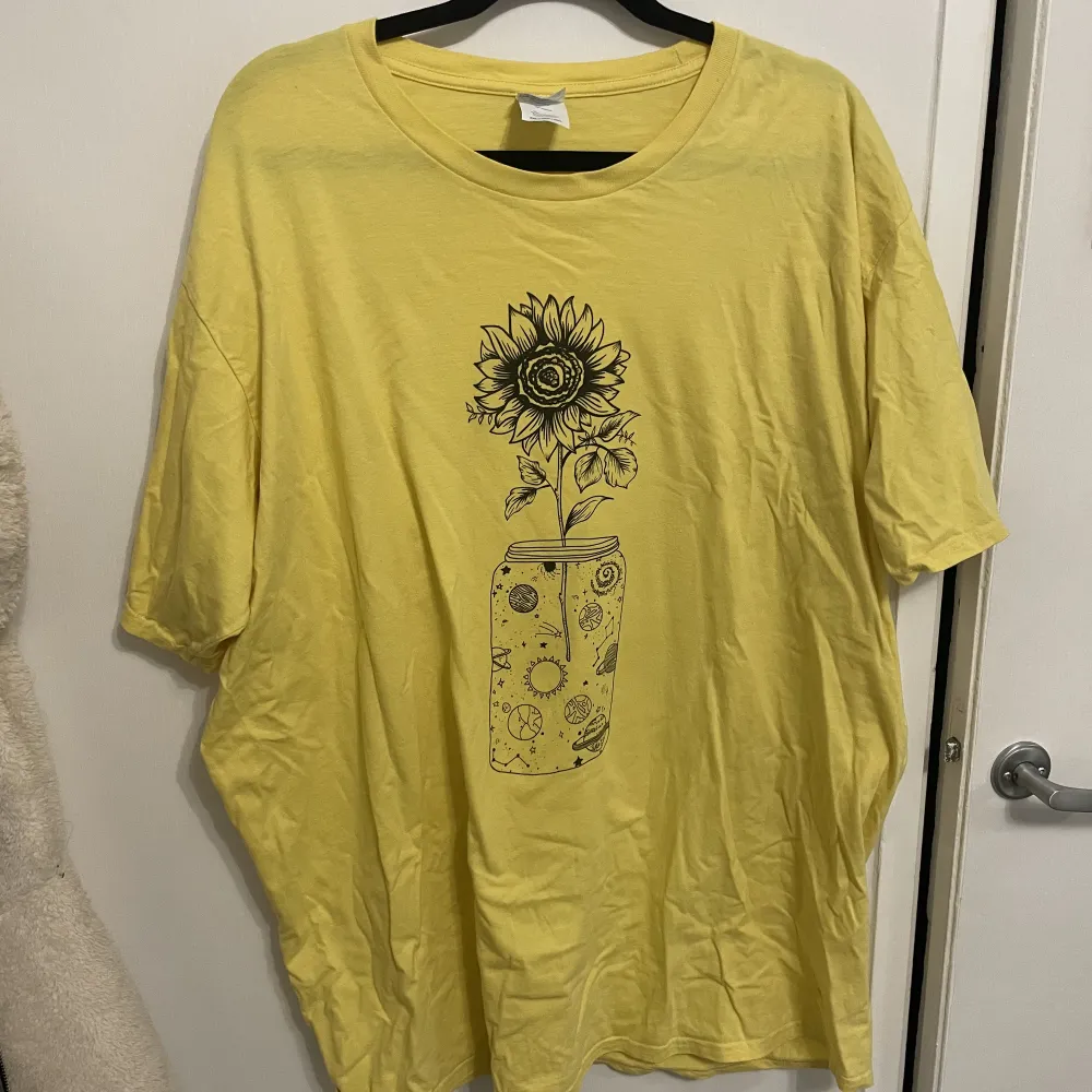 Somrig gul tröja med ett tryck av en blomma.. T-shirts.